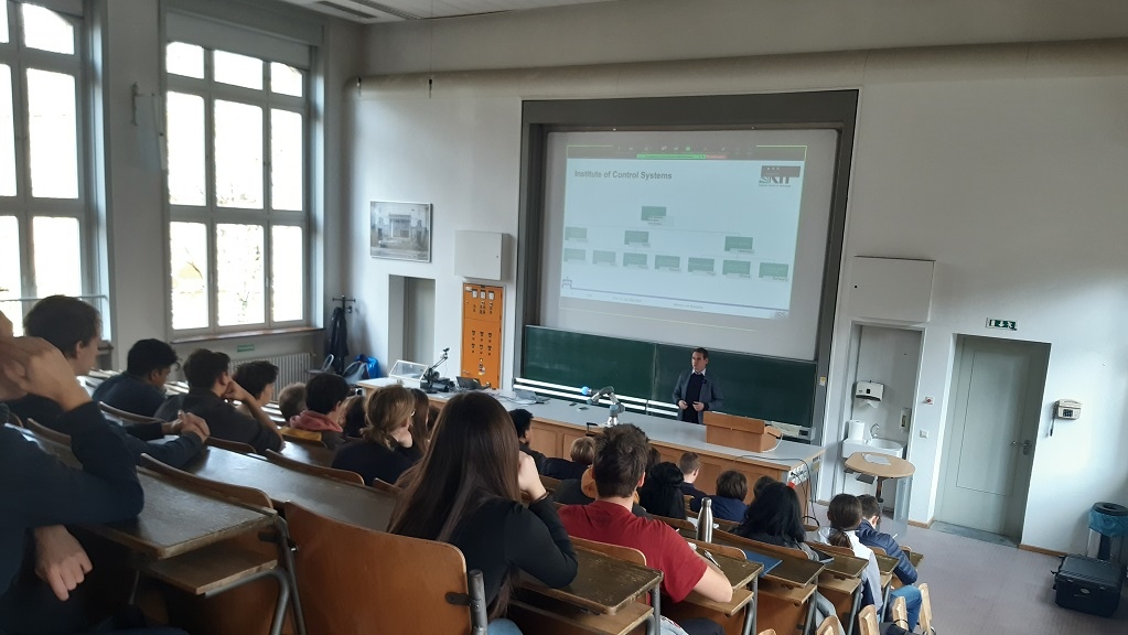 Gefüllter Hörsaal mit Blick nach vorne auf Präsentation und Professor 